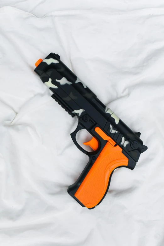 a toy gun laying on top of a bed, orange and black, gen z, camouflage, looking down from above