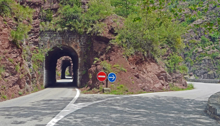 there is a tunnel on the side of the road, a picture, les nabis, rock arches, road street signs, in between a gorge, caulicoli