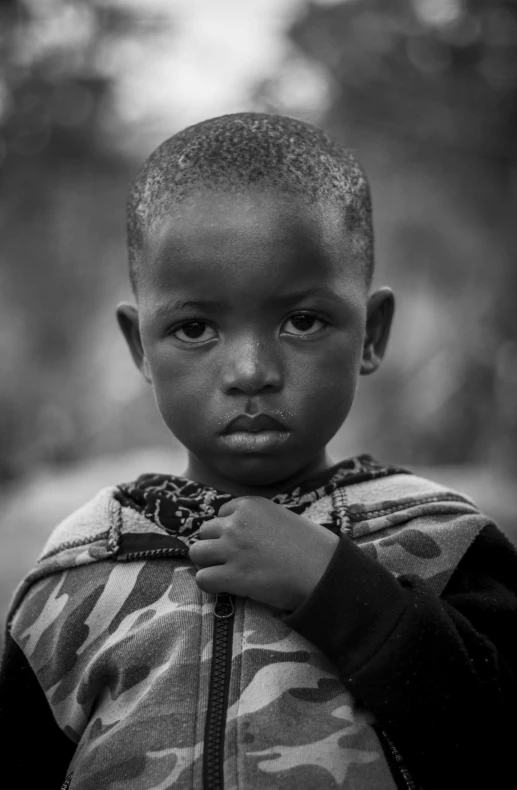 a black and white photo of a young boy, by Joze Ciuha, masai, over his shoulder, 4yr old, looking content