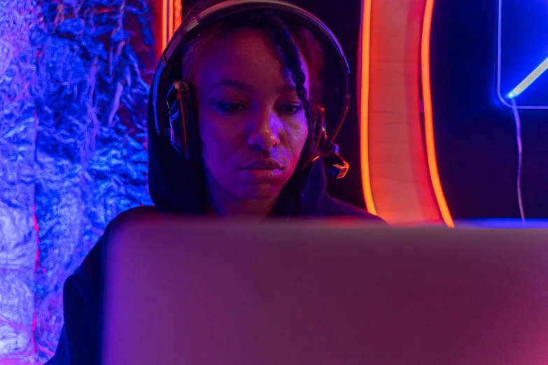 a woman sitting in front of a laptop wearing headphones, pexels, afrofuturism, blue and orange rim lights, gaming room, avatar image, mid shot photo