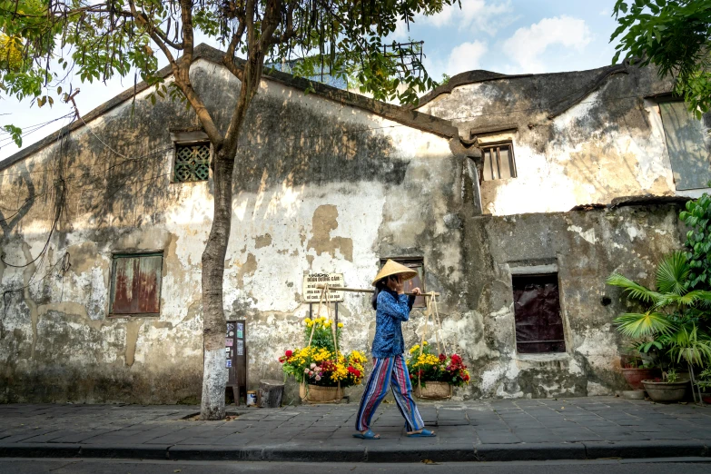 a woman walking down a street past a building, inspired by Cui Bai, lush surroundings, pith helmet, 2019 trending photo, conde nast traveler photo