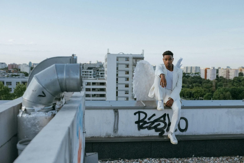 a man sitting on top of a building, white wings, berlin fashion, neo soul, wearing white suit