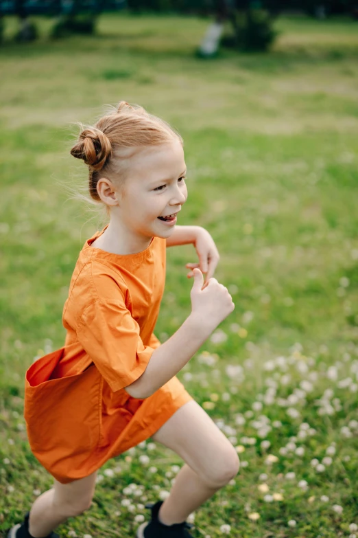 a little girl in an orange dress playing with a frisbee, inspired by Elsa Beskow, pexels contest winner, happening, girl with messy bun hairstyle, a still of a happy, sprinting, on the field