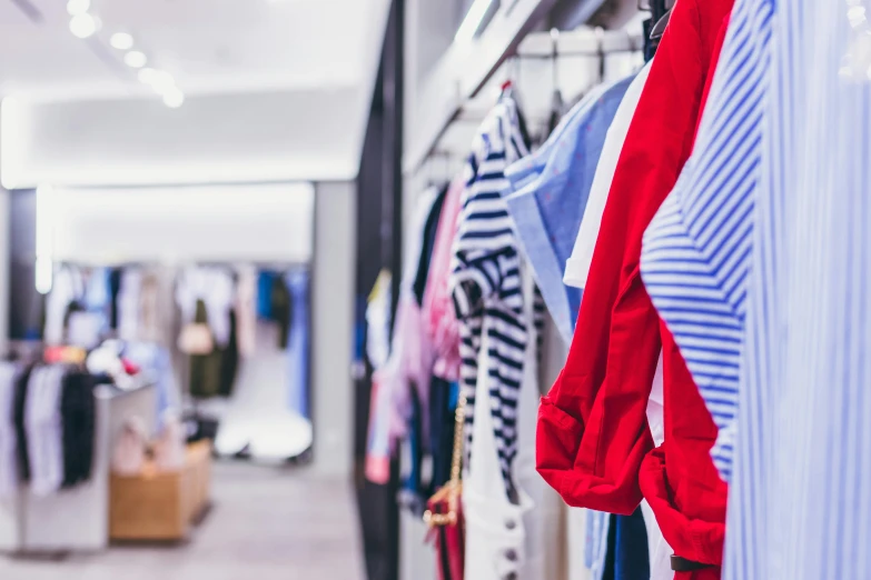 a row of clothes hanging on a rack in a store, trending on pexels, brand colours are red and blue, mall background, looking across the shoulder, sarenrae