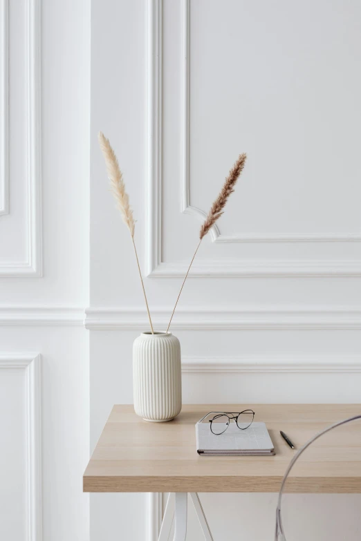 a white vase sitting on top of a wooden table, inspired by Constantin Hansen, trending on pexels, reeds, in a white boho style studio, a pair of ribbed, white reading glasses
