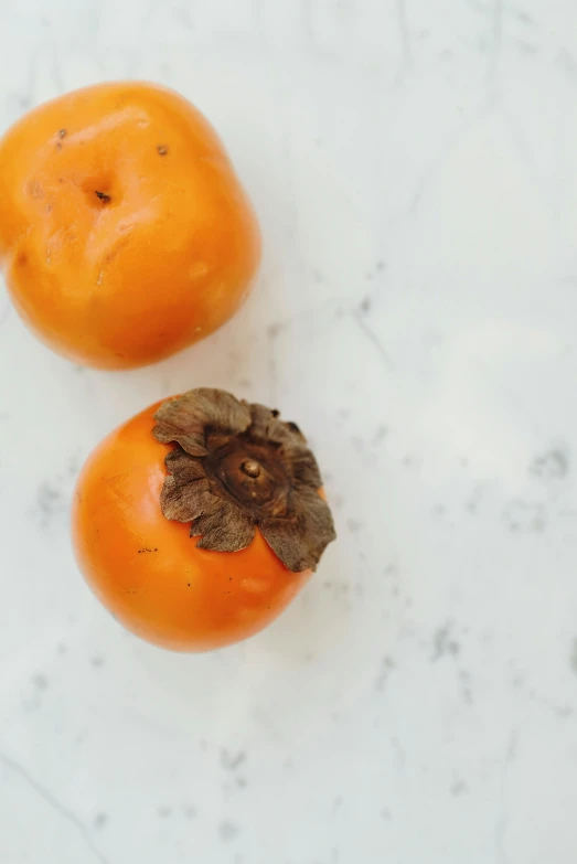 two persimmonan sitting next to each other on a table, a still life, by Amelia Robertson Hill, trending on unsplash, dead fruits, orange fluffy spines, poppy, high angle close up shot
