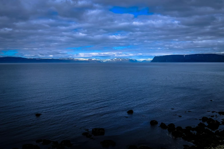 a large body of water under a cloudy sky, a picture, by Else Alfelt, pexels contest winner, hurufiyya, snowy fjord, dark blue water, youtube thumbnail, 8k hdr morning light