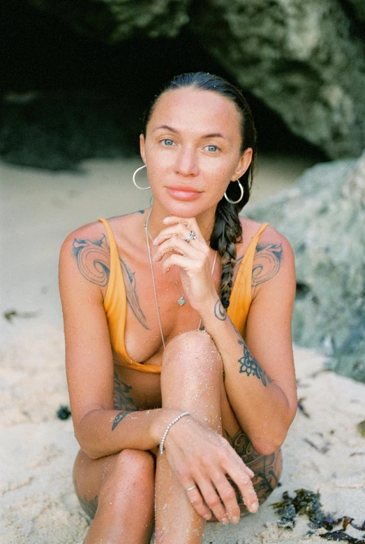 a woman sitting on top of a sandy beach, a tattoo, headshot, tan skin, bali, upper body and face