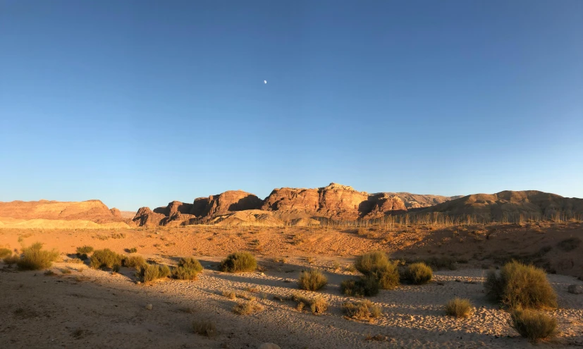 a view of a desert with mountains in the background, a picture, hurufiyya, big moon on the right, panoramic view, /r/earthporn, evening sunlight