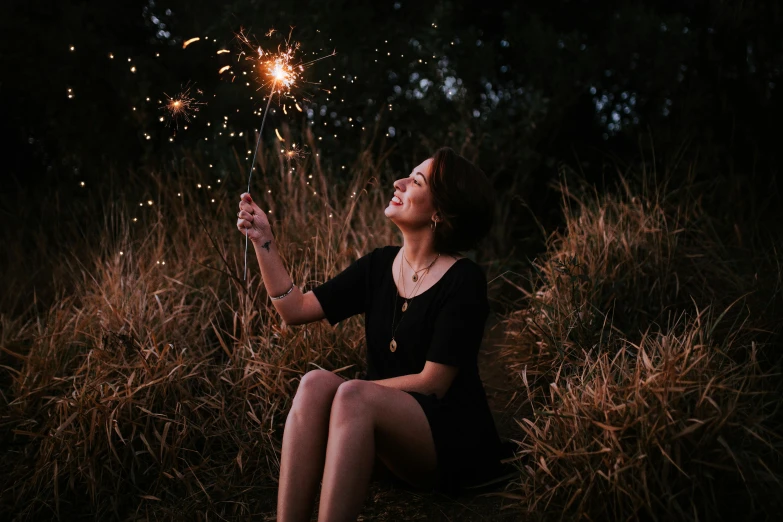 a woman sitting in a field holding a sparkler, pexels contest winner, wearing a dark dress, looking happy, profile image, girls