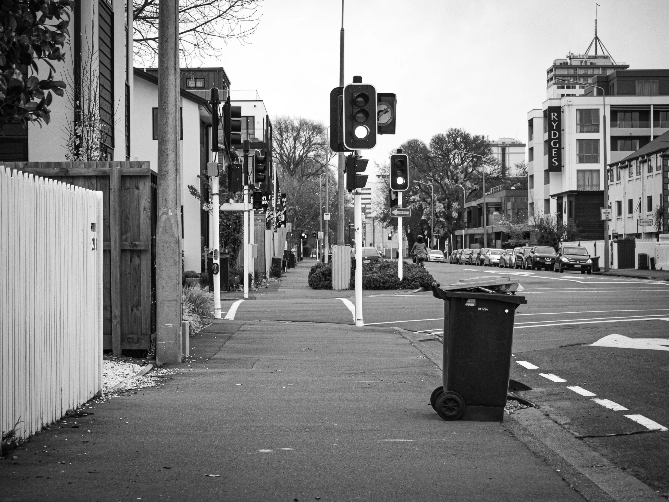 a trash can sitting on the side of a road, a black and white photo, by Niko Henrichon, unsplash, wellington, traffic lights, old cmputers on the sidewalk, busy small town street