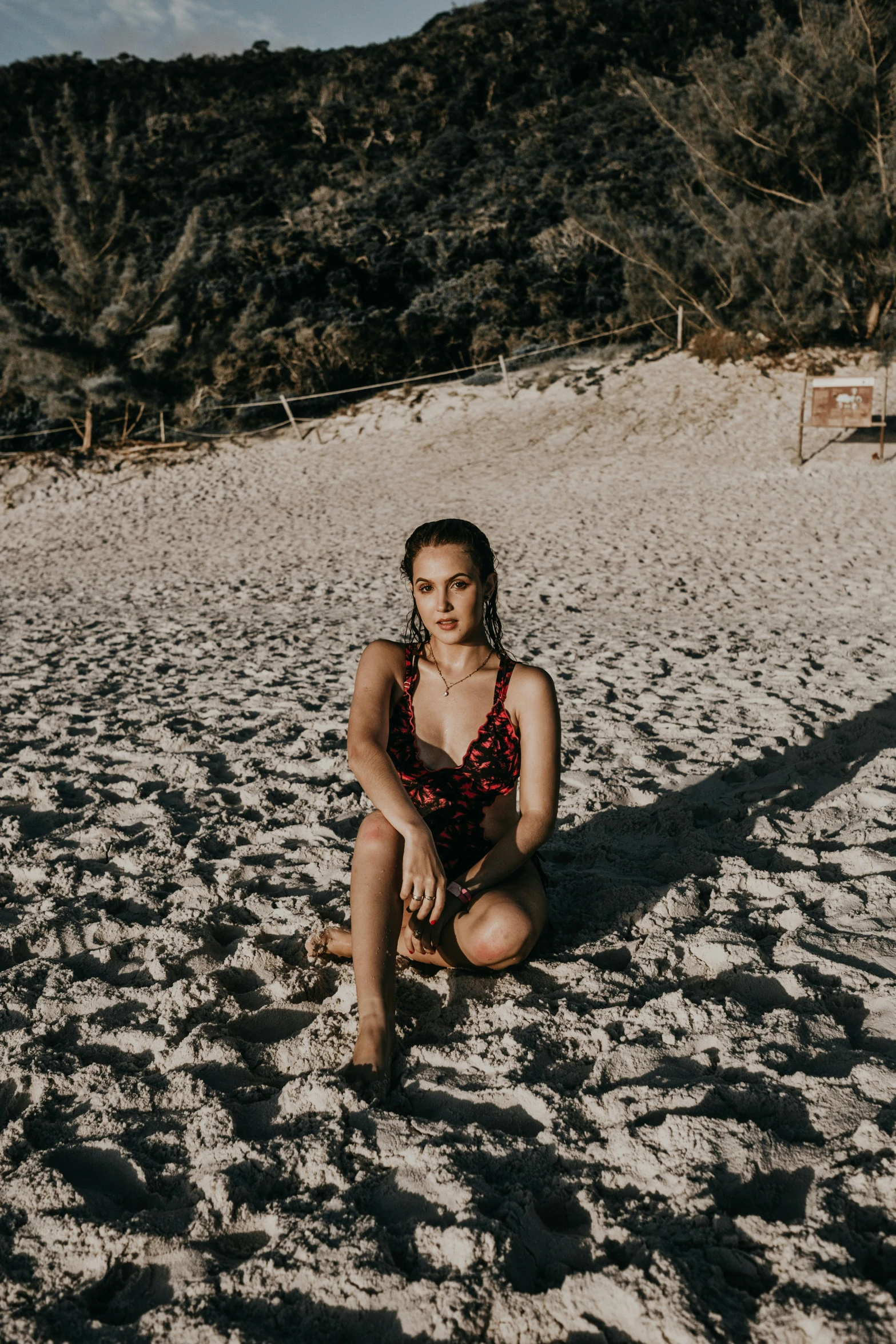 a woman sitting on top of a sandy beach, posing for a picture