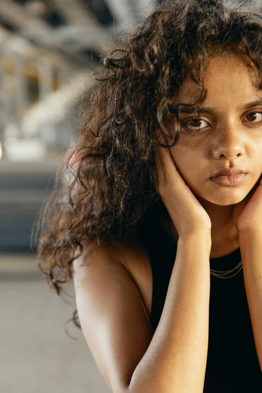 a woman sitting at a table with her hands on her face, trending on pexels, renaissance, black teenage girl, proud serious expression, young middle eastern woman, curly bangs and ponytail