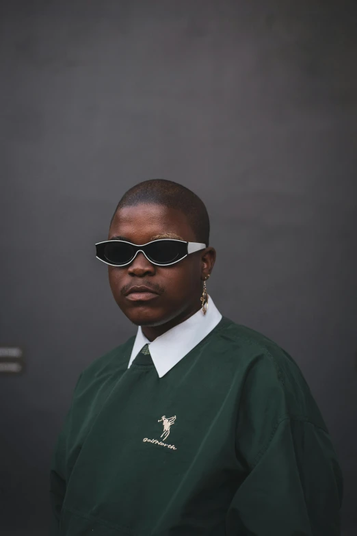 a woman standing in front of a black door, an album cover, by Attila Meszlenyi, trending on unsplash, afrofuturism, in a dark green polo shirt, implanted sunglasses, at new york fashion week, attractive androgynous humanoid