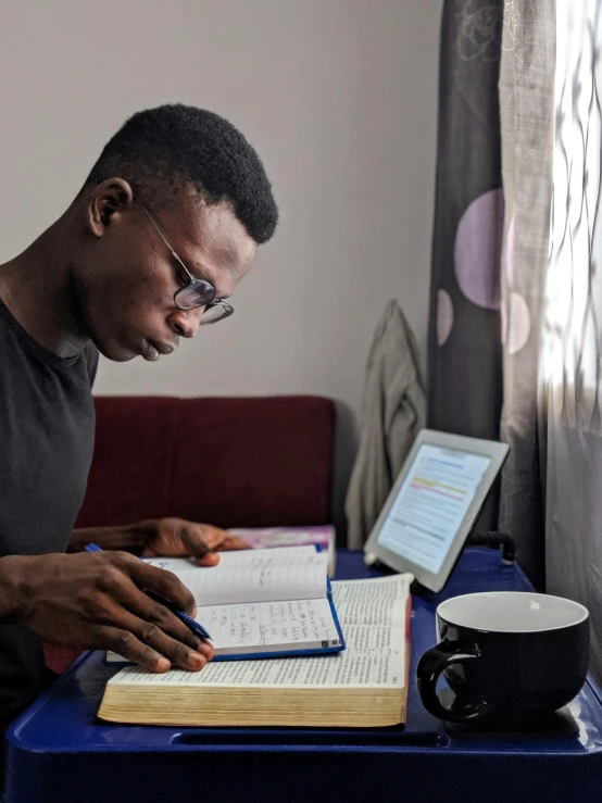 a man sitting at a table with a laptop and a book, pexels, academic art, emmanuel shiru, studyng in bedroom, holding spell book, gif