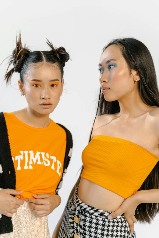 a couple of women standing next to each other, trending on unsplash, toyism, wearing yellow croptop, resembling a mix of grimes, photoshoot for skincare brand, orange pupils