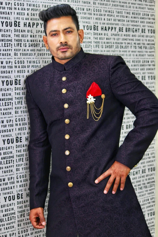 a man standing in front of a wall with words on it, a portrait, inspired by Saurabh Jethani, pexels, renaissance, a purple suit jacket, dark ornate royal robes, groom, dressed in a jodhpuri suit