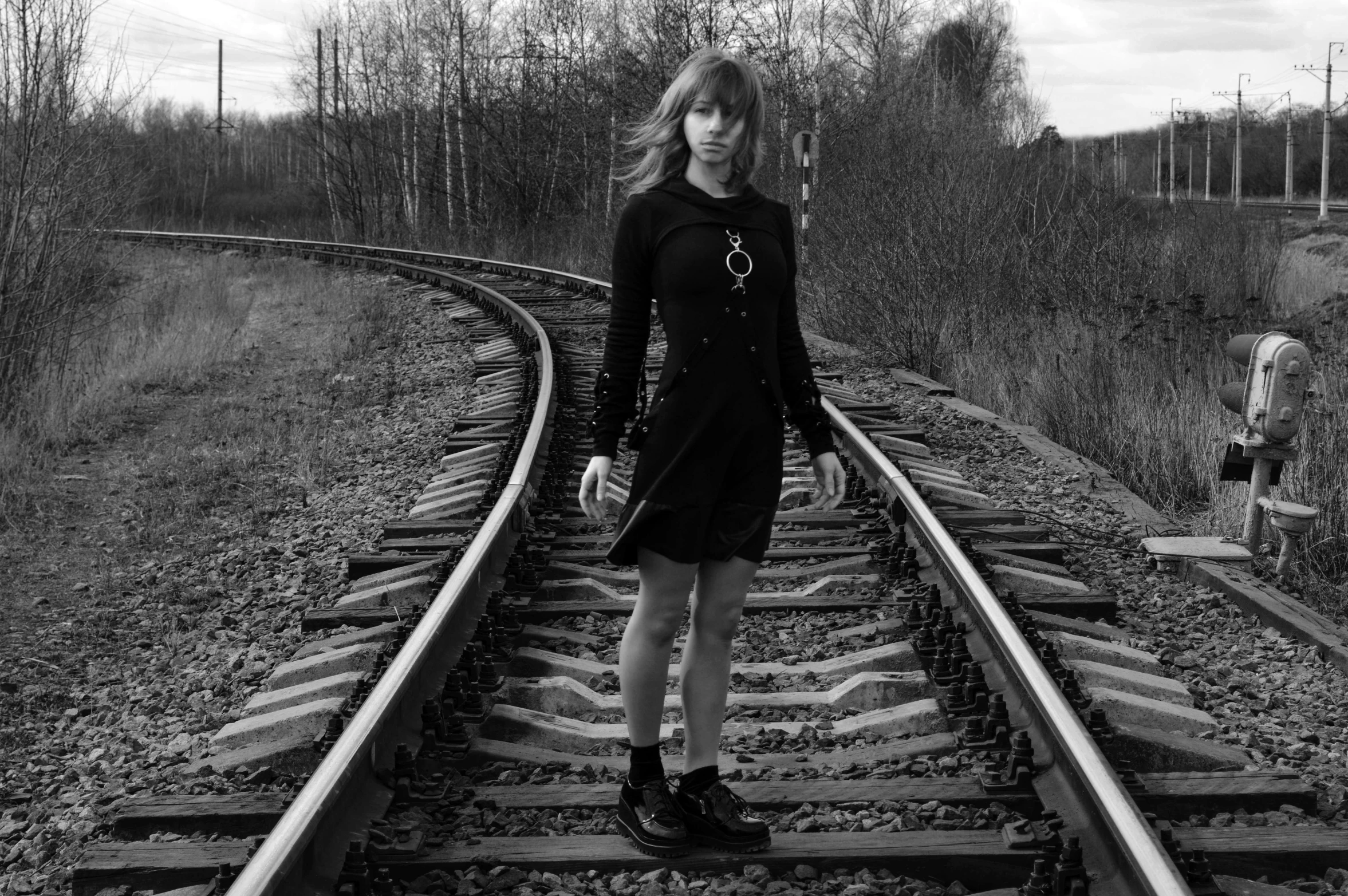 a woman in a black dress standing on a train track, an album cover, inspired by August Sander, surrealism, orthodox symbolism diesel punk, she wears boots, teenage girl, monochrome:-2