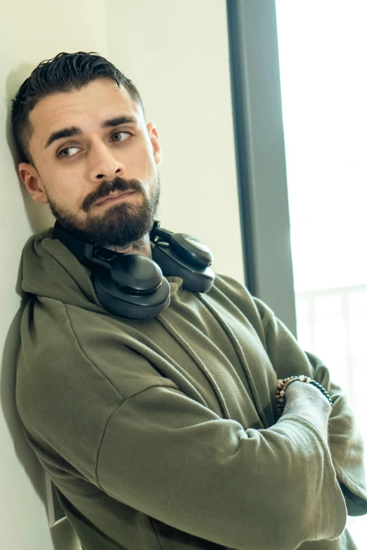 a man wearing headphones leaning against a wall, inspired by Ludovit Fulla, antipodeans, scruffy looking, wearing camo, lgbtq, with a small beard