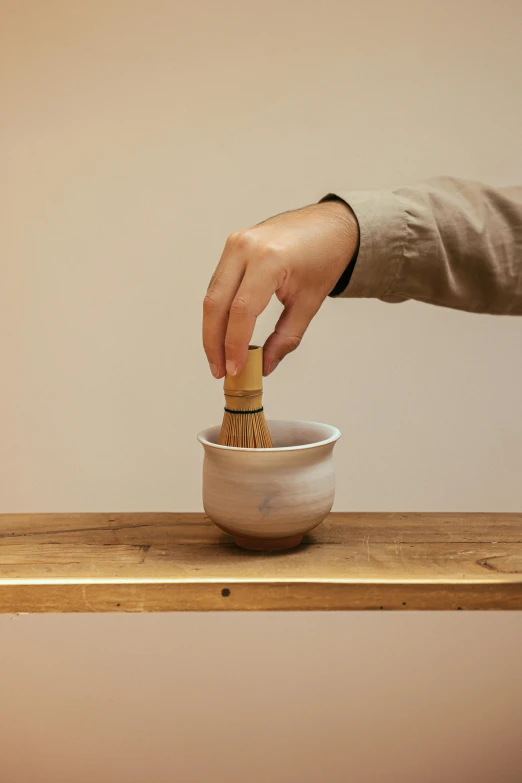 a person stirring something in a bowl on a wooden table, inspired by Kanō Shōsenin, large brush, ochre, vanilla, large tall