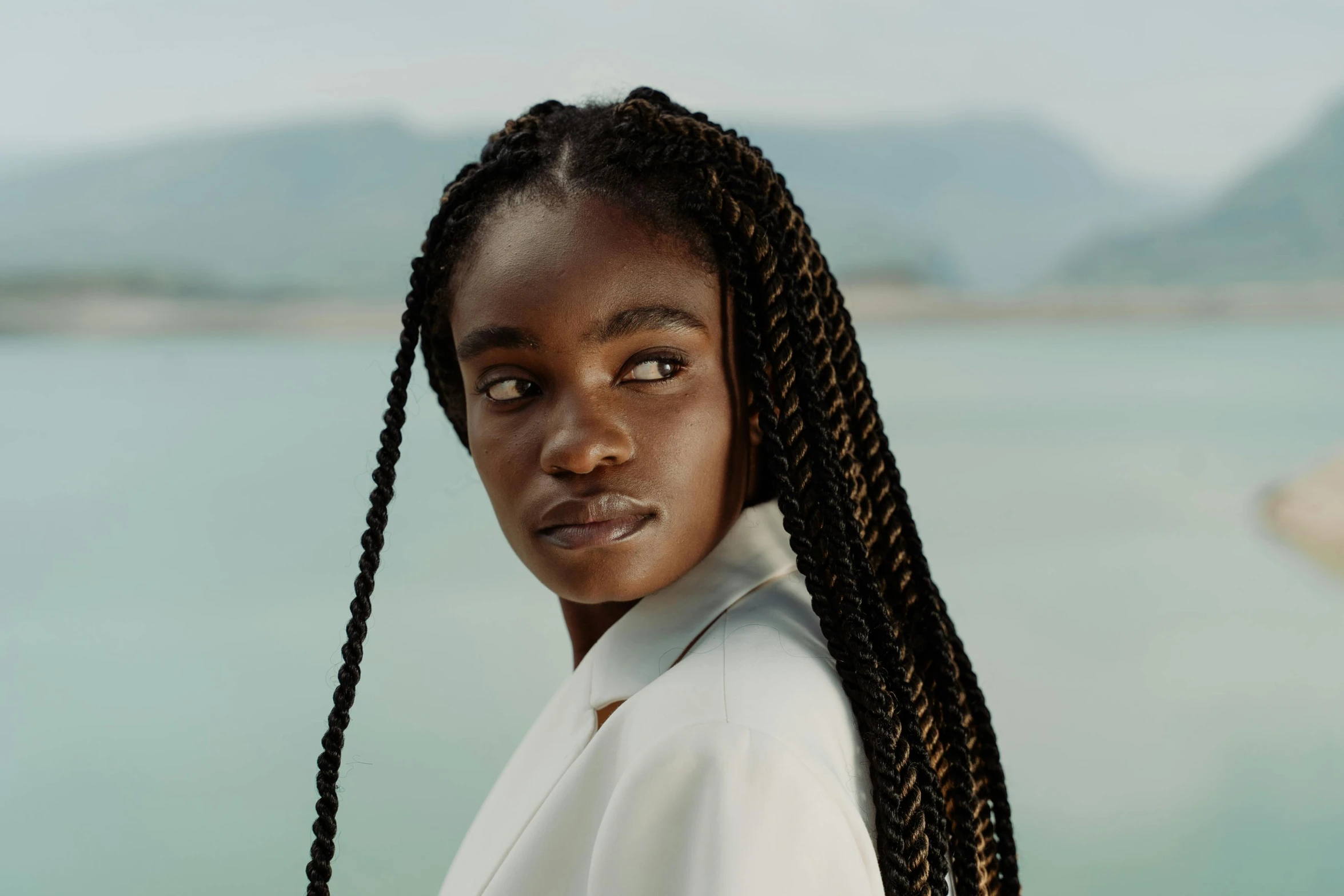 a woman standing in front of a body of water, pexels contest winner, hyperrealism, box braids, avatar image, sophisticated young woman, off - white collection