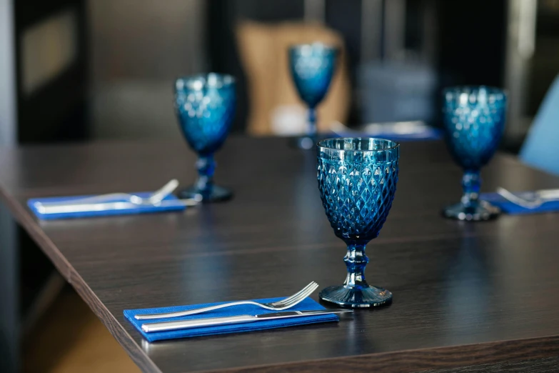 a blue glass goblet sitting on top of a wooden table, sitting at a table, long table, ready for a meeting, picton blue