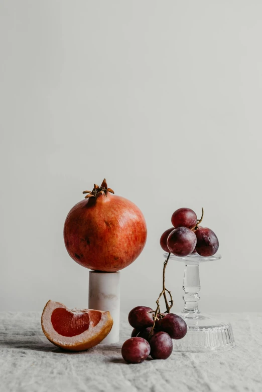 a bunch of grapes and a pomegranate on a table, a still life, trending on pexels, white marble interior photograph, standing, kailee mandel, refined editorial photograph