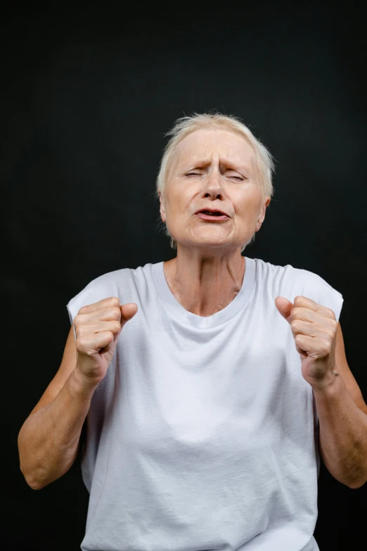 an older woman standing in front of a black background, wearing a tee shirt and combats, frustrated face, large muscles, non-binary