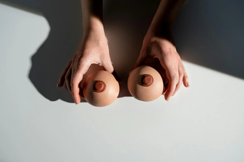 a person holding two eggs in their hands, an album cover, inspired by Hans Bellmer, unsplash, purism, terracotta, large breasts size, eye level view, minimalist photorealist