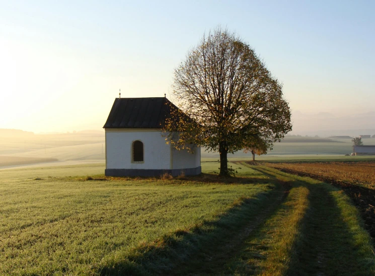a small white building sitting on top of a lush green field, inspired by Otakar Sedloň, romanticism, at sunset in autumn, ribbon chapel, profile picture 1024px, brown