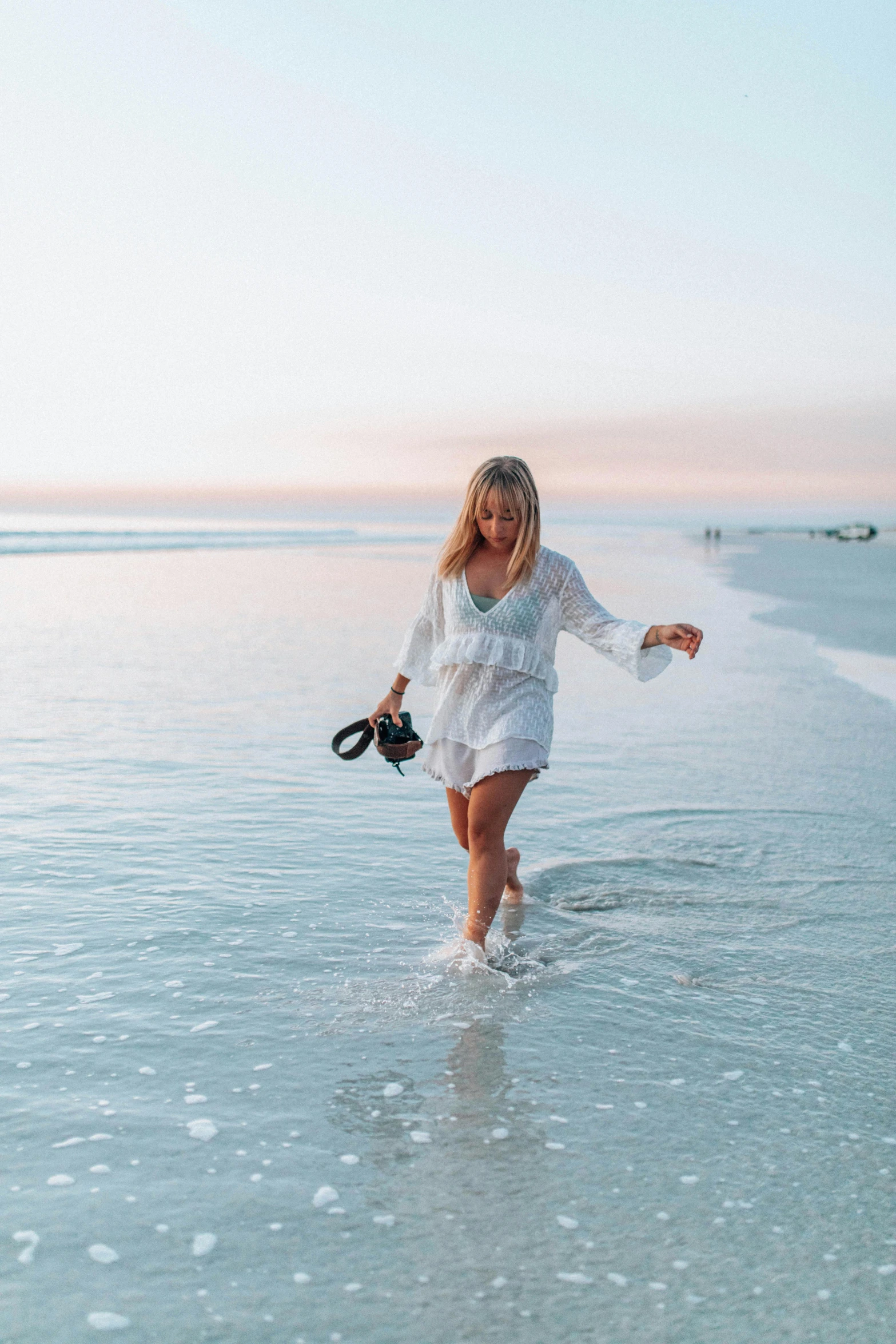 a woman walking on the beach with a camera, soft white glow, in water, blonde, kailee mandel