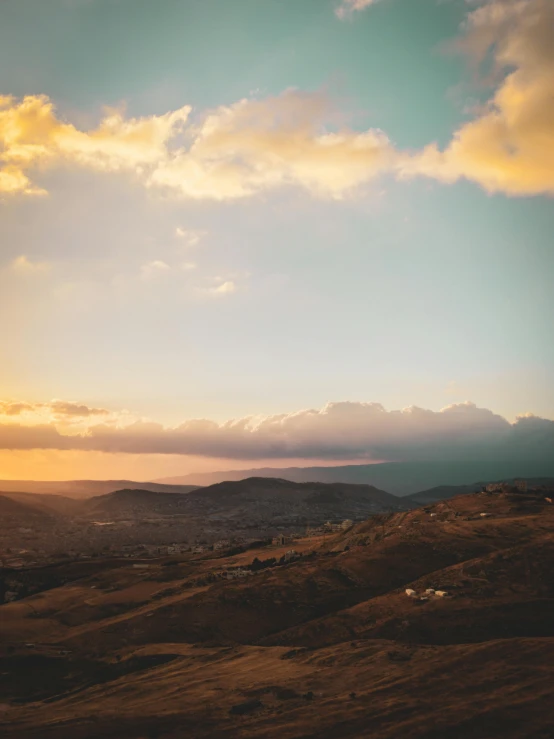 a person standing on top of a hill under a cloudy sky, unsplash contest winner, renaissance, distant town in valley and hills, golden hues, reunion island landscape, agrigento