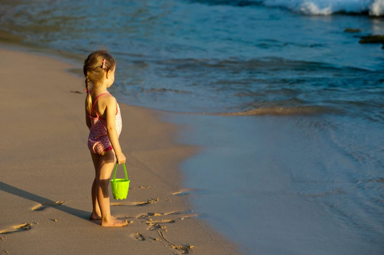 a little girl standing on top of a beach next to the ocean