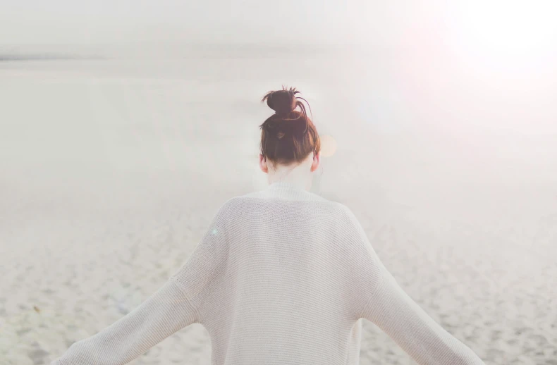 a woman standing on top of a sandy beach, pexels contest winner, minimalism, wearing a white sweater, girl with messy bun hairstyle, pastel faded effect, her back is to us