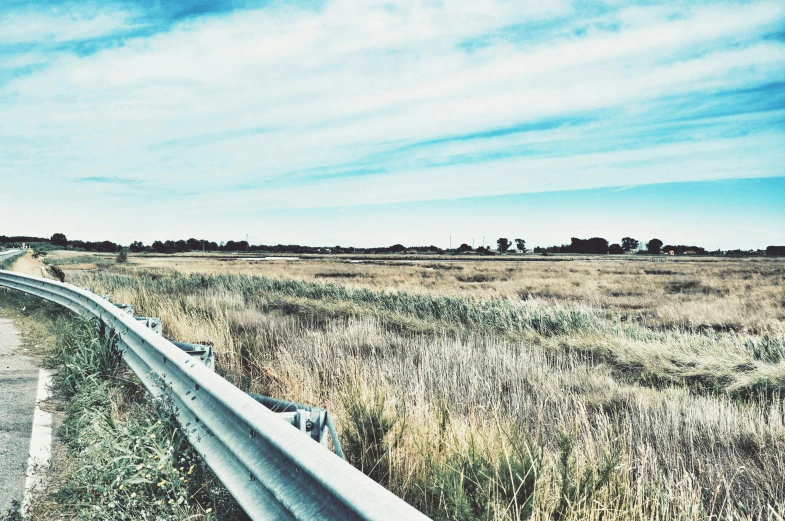 a long metal guard rail on the side of a road, an album cover, unsplash, land art, marshes, background image, clear blue sky vintage style, enhanced photo