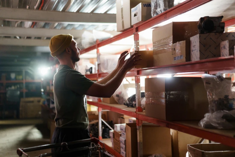 a man standing in front of a shelf filled with boxes, industrial lighting, working hard, avatar image, vendors