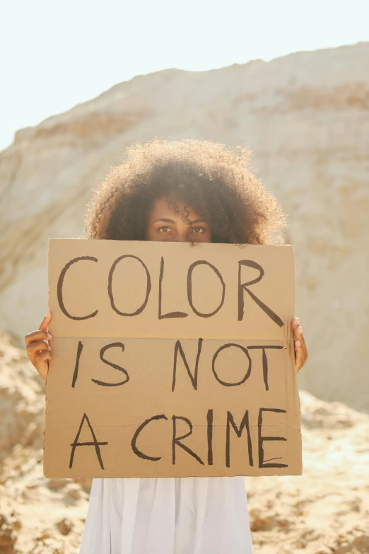 a woman holding a sign that says color is not a crime, a colorized photo, trending on pexels, color field, brown skin like soil, black in, contain, afro