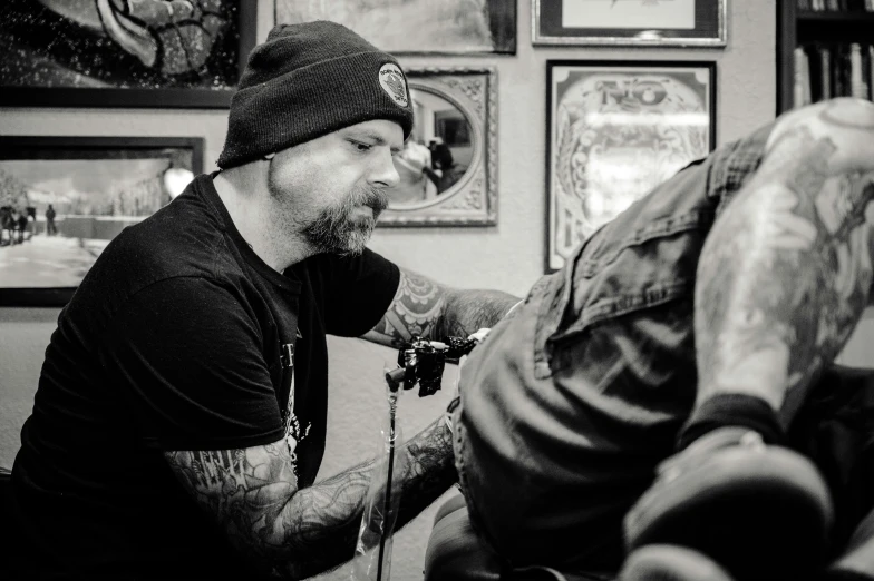 a man getting a tattoo on another man's arm, a tattoo, by Brian 'Chippy' Dugan, sitting in his chair. intricate, black ink, bokeh. brian spilner, full head shot