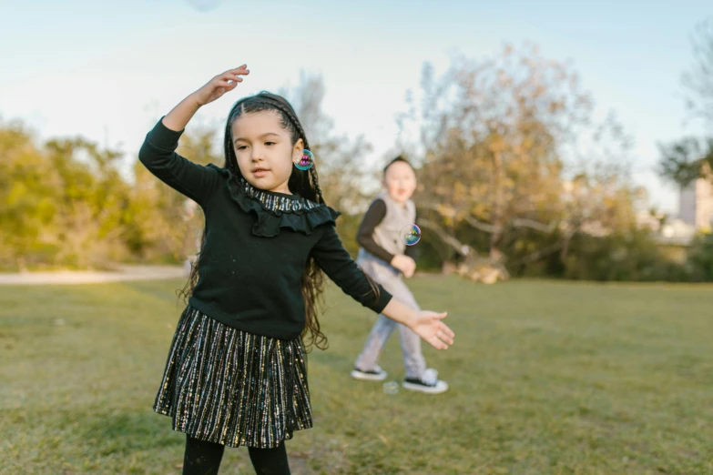 a little girl standing on top of a lush green field, an album cover, pexels contest winner, dancing with each other, black, manuka, at a park