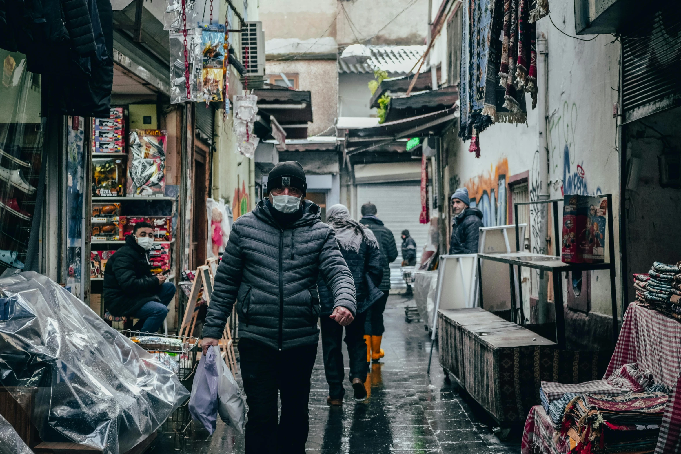 a person wearing a face mask walking down a street, by Julia Pishtar, pexels contest winner, inside an arabian market bazaar, snow weather, samarkand, wet market street