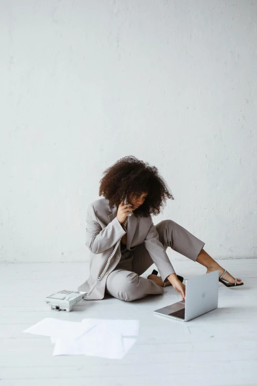 a woman sitting on the floor using a laptop, by Nina Hamnett, trending on pexels, minimalism, tan suit, afro tech, grey suit, frustration