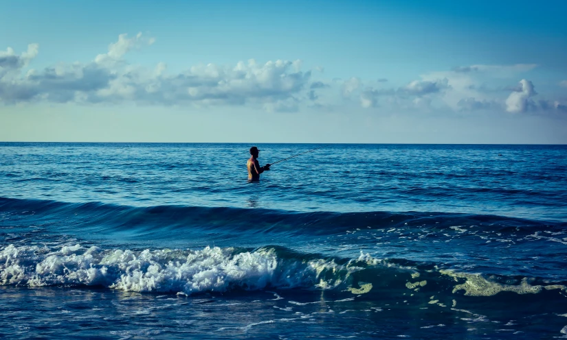 a man standing on top of a surfboard in the ocean, unsplash, blue hues, people swimming, coming ashore, fishing