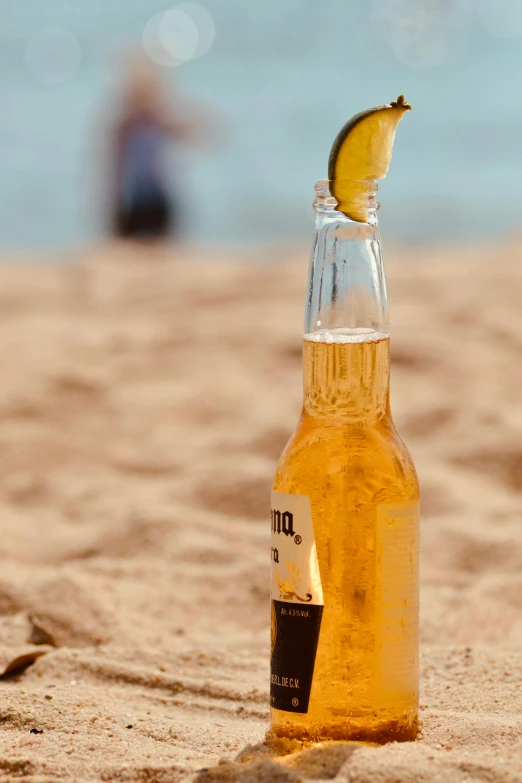 a bottle of beer sitting on top of a sandy beach, on the ocean