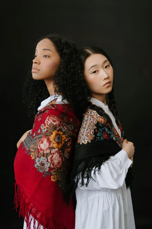 a couple of women standing next to each other, an album cover, trending on pexels, cloisonnism, shawl, jingna zhang, mixed race, fashion portrait