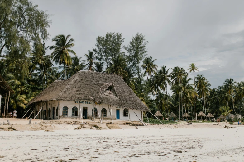 a hut sitting on top of a sandy beach, by Emma Andijewska, unsplash contest winner, hurufiyya, palm trees outside the windows, whitewashed buildings, unmistakably kenyan, 1970s photo