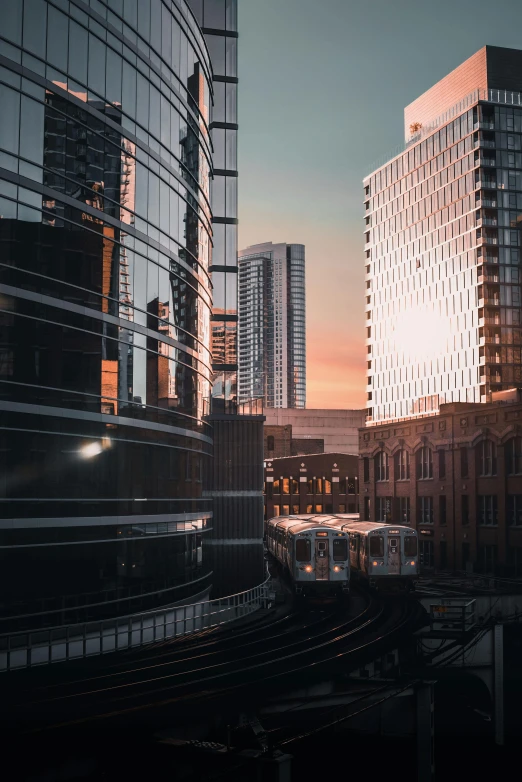 a train traveling through a city next to tall buildings, by Robbie Trevino, unsplash contest winner, chicago, light reflection, late afternoon light, buildings made out of glass