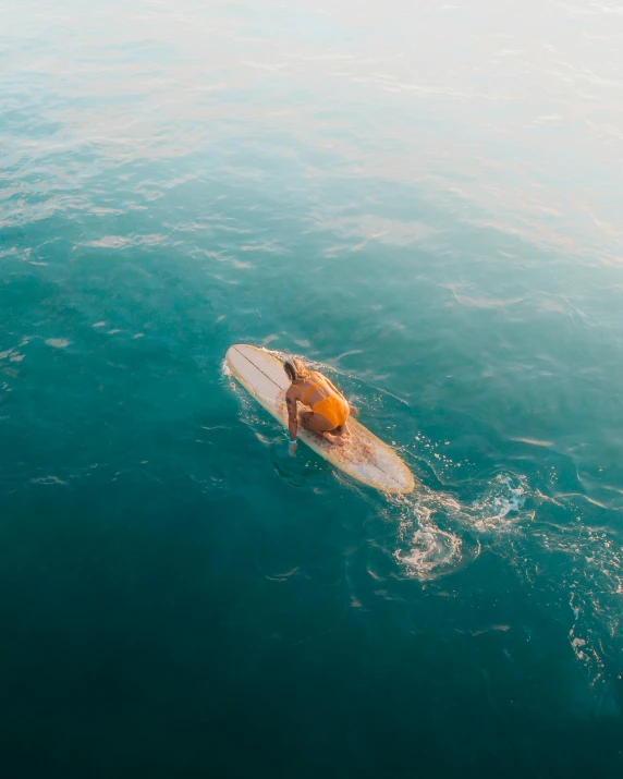 a person riding a surfboard on top of a body of water, looking down from above, in the evening, in the sun