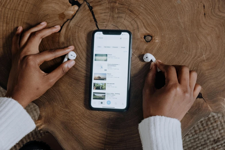 a person sitting at a table with a cell phone and headphones, a picture, trending on pexels, airpods, aerogel ios ui concept, a wooden, thumbnail