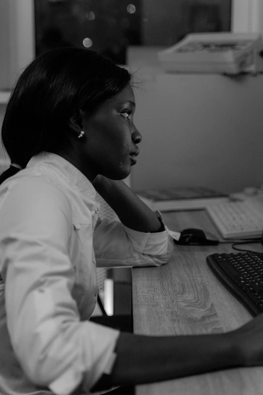 a woman sitting at a desk using a computer, a black and white photo, inspired by Chinwe Chukwuogo-Roy, flickr, happening, looking off to the side, programming, early evening, professional profile picture