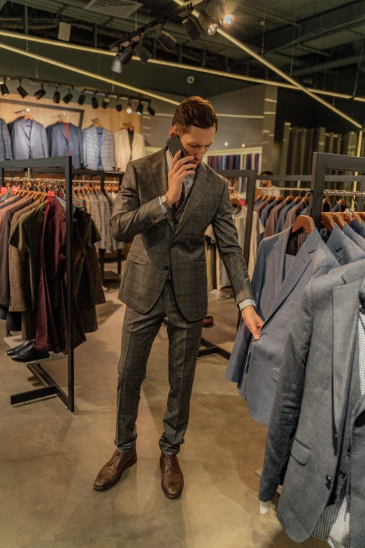 a man in a suit standing in a clothing store, by Jan Tengnagel, instagram, happening, figuring, grey suit, looking at his phone, performance